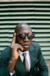Man in suit and sunglasses with hand on temple.